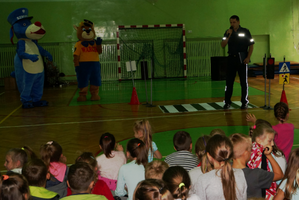 Policjant przedstawia dzieciom maskotkę śląskiej policji Sznupka