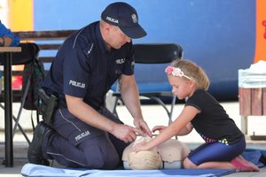 Policjant przy użyciu fantoma pokazuje dziewczynce zasady udzielania pierwszej pomocy przedmedycznej.