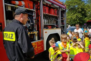 Wóz strażacki obok którego stoi strażak i dzieci