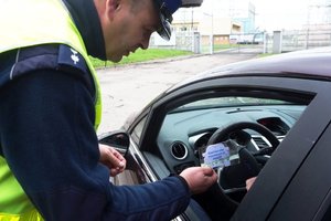 Policjant wręcza kierowcy zapachową zawieszkę.