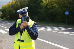 Policjant przy użyciu laserowego miernika kontroluje prędkość pojazdów.