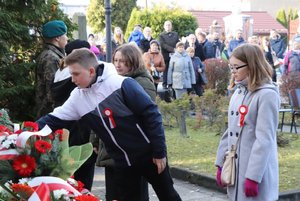Chłopiec w towarzystwie dziewczynki składa kwiaty przed Pomnikiem Niepodległości.