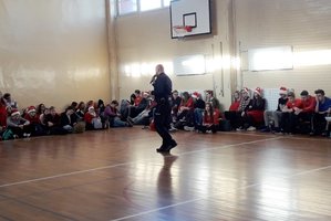 Policjant prowadzi prelekcje dla młodzieży. Spotkanie odbyło się na sali gimnastycznej. Uczniowie siedzą wokół prelegenta.