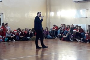 Przedstawiciel Allegro.pl prowadzi prelekcje dla młodzieży. Spotkanie odbyło się na sali gimnastycznej. Uczniowie siedzą wokół prelegenta.