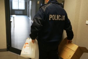 Policjant niosący płyn do dezynfekcji oraz kartonowe pudełko.