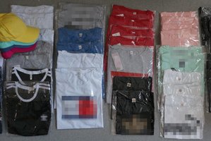 Na zdjęciu widoczne zabezpieczone ubrania: zapakowane w folię koszulk oraz czapki z daszkiem.