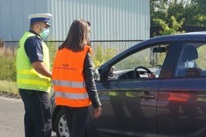 Widoczny policjant i pracownica PKP rozmawiający z kierowcą siedzącym w zatrzymanym pojeździe.