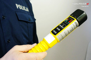 Częściowo widoczny policjant trzymający w ręku urządzenie do badania stanu trzeźwości.