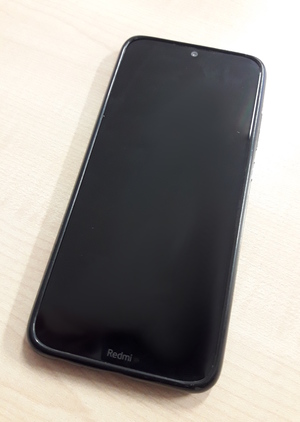 Na zdjęciu widoczny czarny smartfon. W dolnej jego części widnieje napis REDMI.