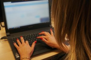 Widoczna na zdjęciu kobieta pisząca na klawiaturze laptopa.