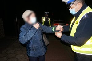 Umundurowany policjant zakłada opaskę odblaskową na rękę przechodzącej kobiecie.