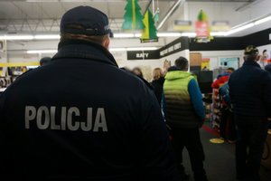 Umundurowany policjant sprawdza, czy klienci sklepu stosują się do zasad bezpieczeństwa