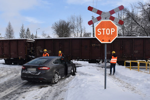 Na zdjęciu widoczny samochód i pociąg towarowy oraz znak stop.