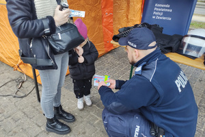 Na zdjęciu widoczny policjant dający dziecku kolorowankę.