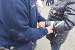 Na zdjęciu widoczny policjant zakładający mężczyźnie na rękę opaskę odblaskową.