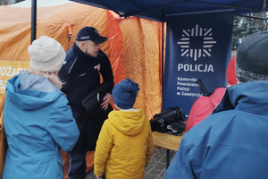 Na zdjęciu widoczny policjant rozmawiający z osobami przy stoisku profilaktycznym.